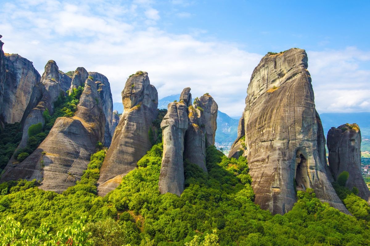 Towering rock formations at Meteora, Greece, surrounded by lush green vegetation under a blue sky.